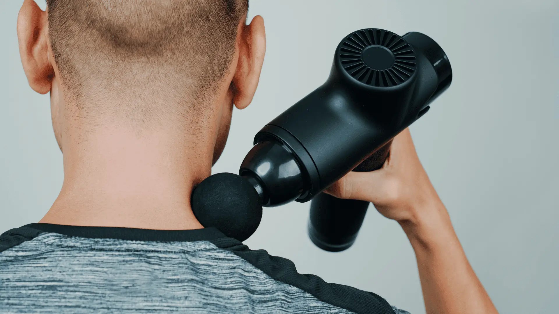 Black massage gun on neck for muscle recovery