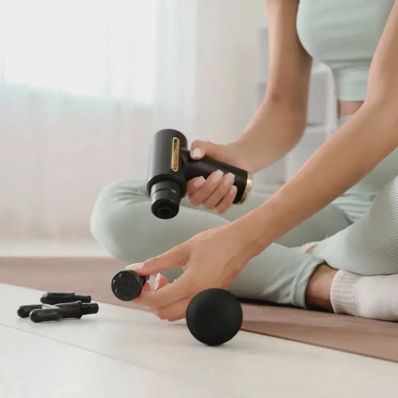 Black massage gun with attachments for muscle recovery, blood flow, and sore muscles