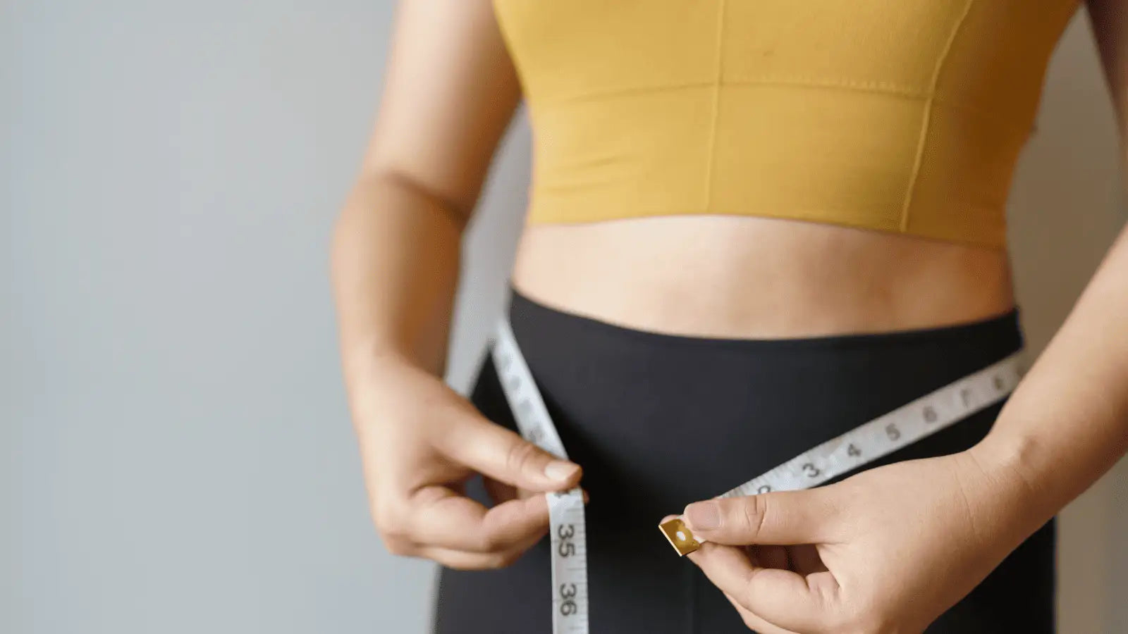 Person measuring waist with tape for fat loss tips in an article about massage guns