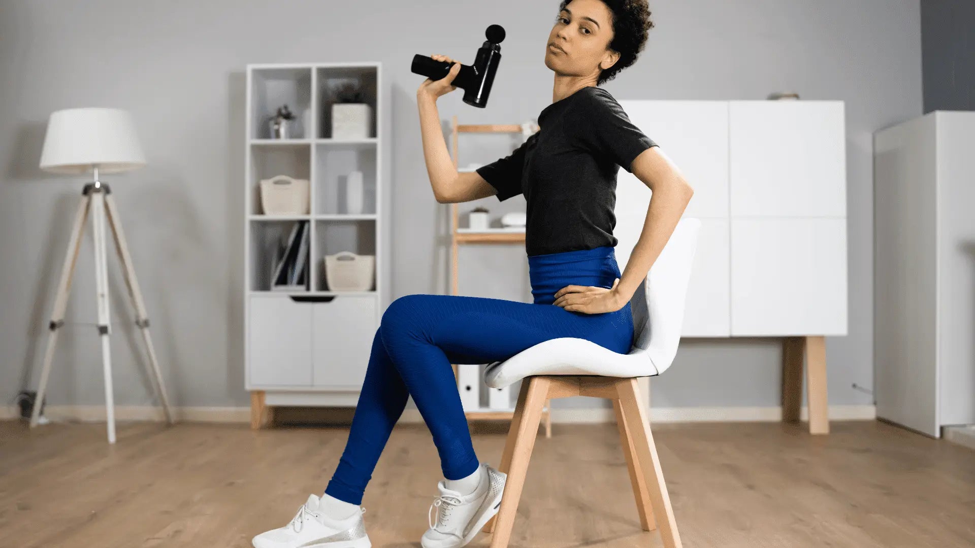 Woman holding a massage gun to relieve muscle soreness highlighting benefits of massage guns