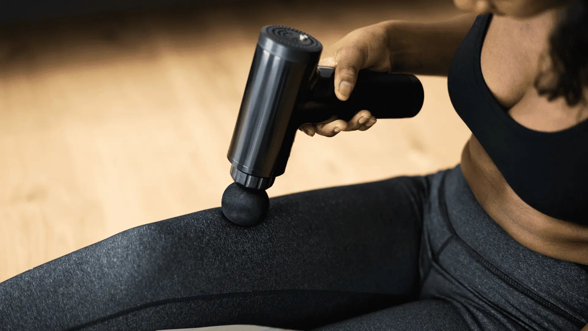 Black massage gun on leg demonstrating how to reset massage guns using reset button