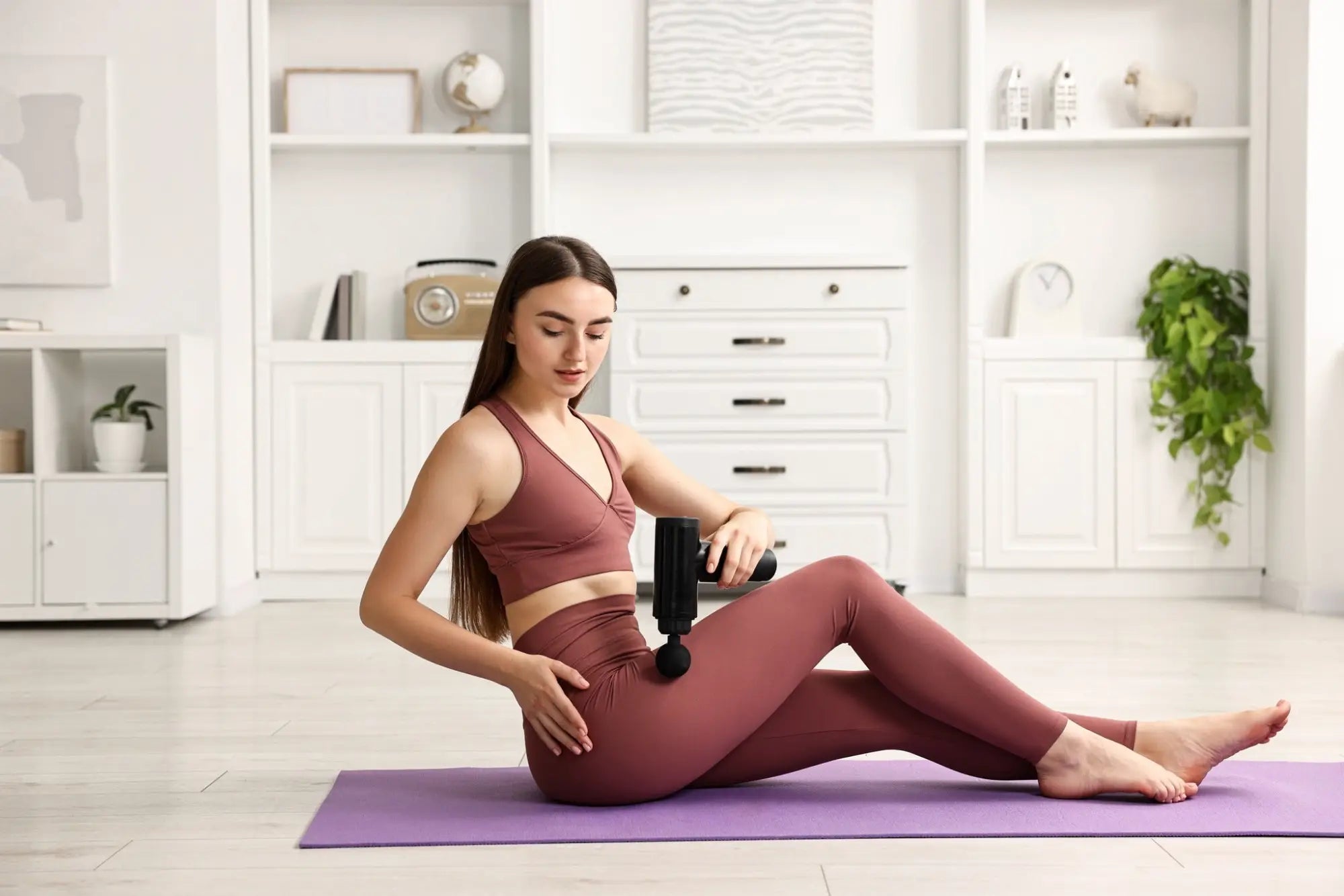 Woman using a massage gun for muscle recovery and relaxation in an article about massage guns